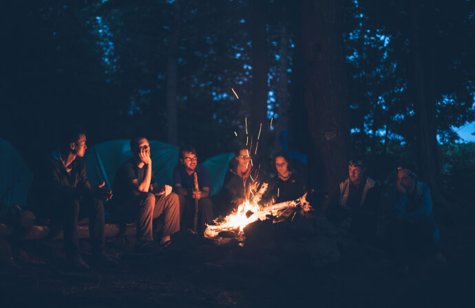 mehrere Personen sitzen bei Nacht um ein großes Lagerfeuer