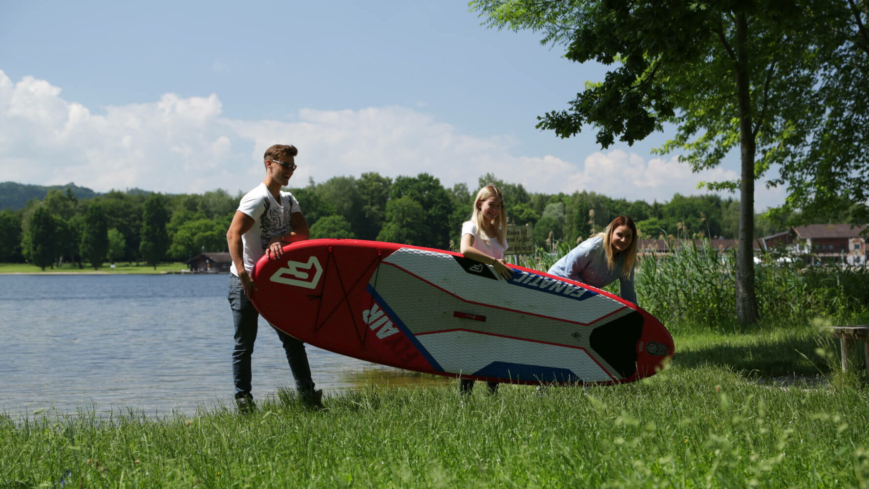 Drei Personen tragen ein Paddleboard am See