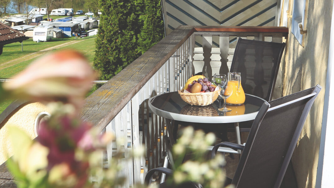 Ein Balkon der Ferienwohnungen mit einem Tisch und zwei Stühlen. Auf dem Tisch steht frisches Obst und Orangensaft