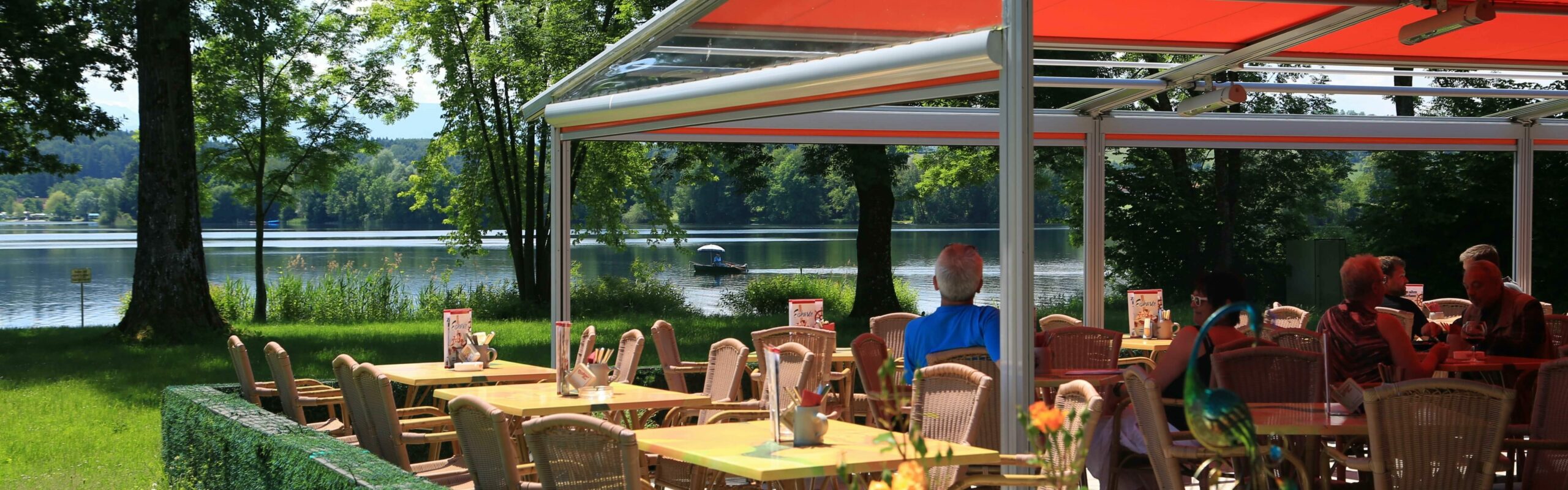Außenansicht der mit einem Schirm überdachten Terrasse des Restaurants zum alten Fährhaus vor dem See.
