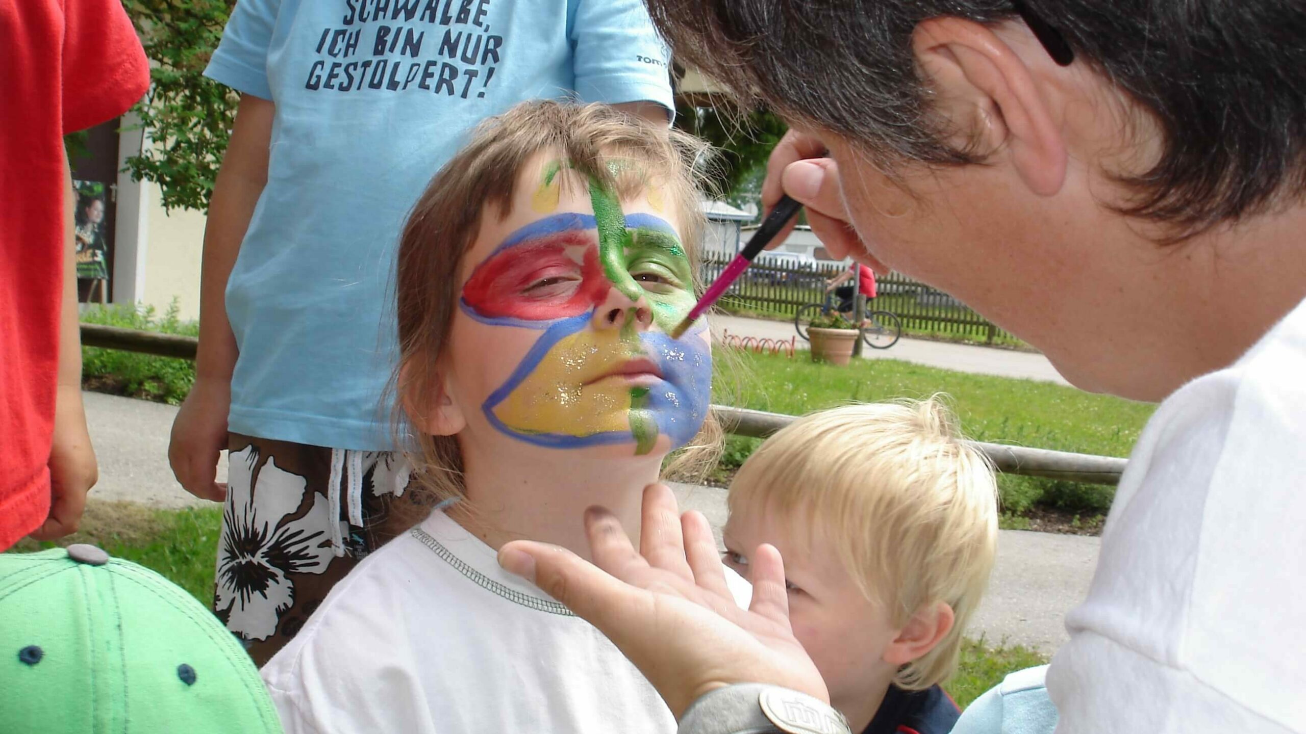 Ein Kind bekommt einen bunten Schmetterling auf das Gesicht gemalt