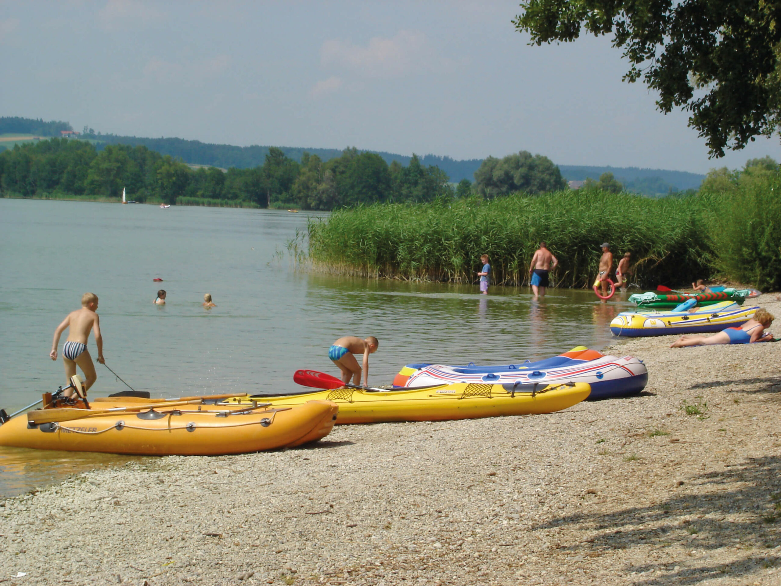 Einige badende Leute und kleine Boote am Kiesstrand des Waginger Sees